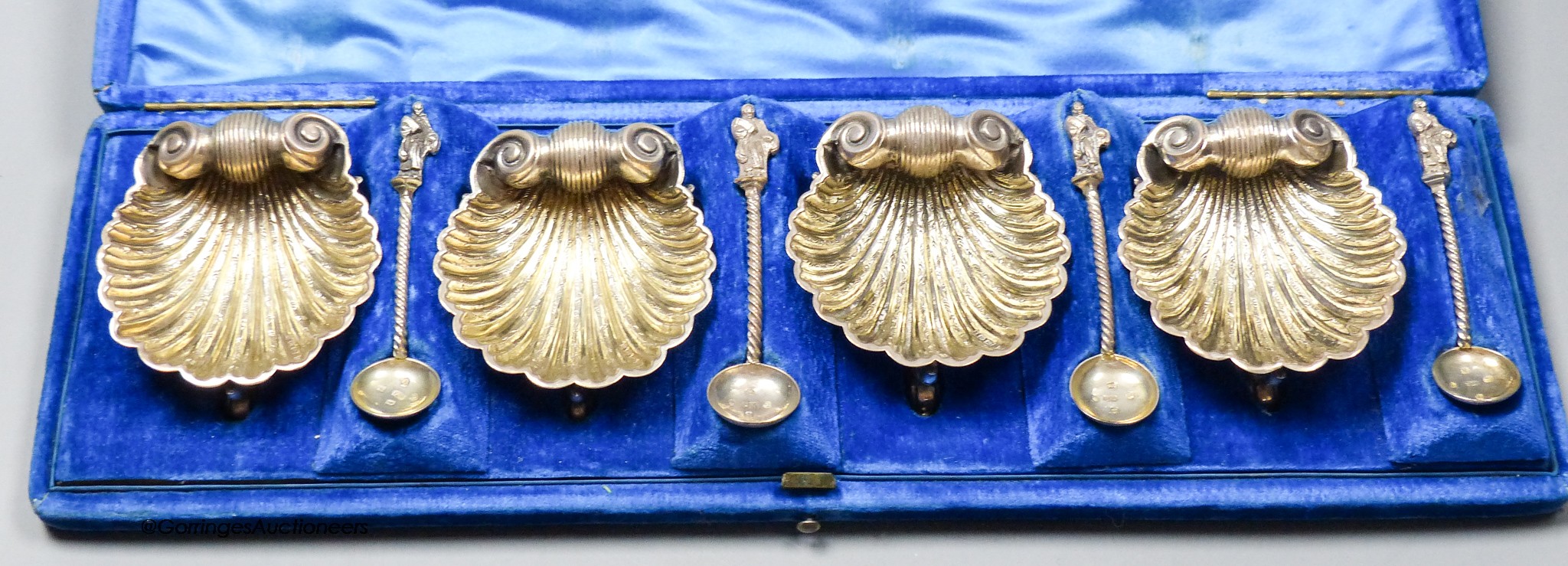 A cased set of four Victorian silver scallop shell salts, on dolphin feet, with four matching apostle salt spoons, Henry Hyde Aston, Birmingham, 1862, 67mm, 6.5oz.